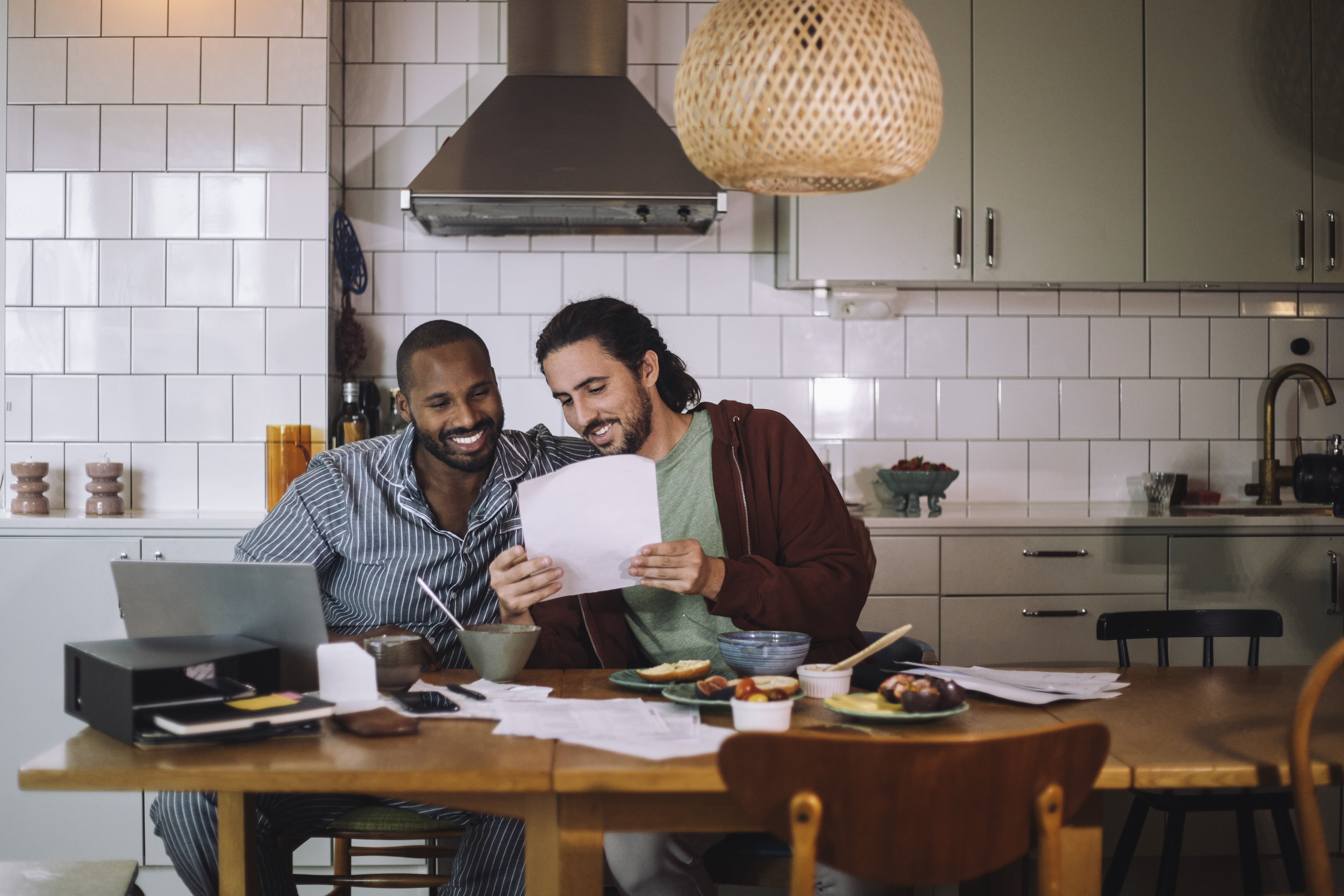 To menn som sitter på kjøkkenet med papirer og en pc