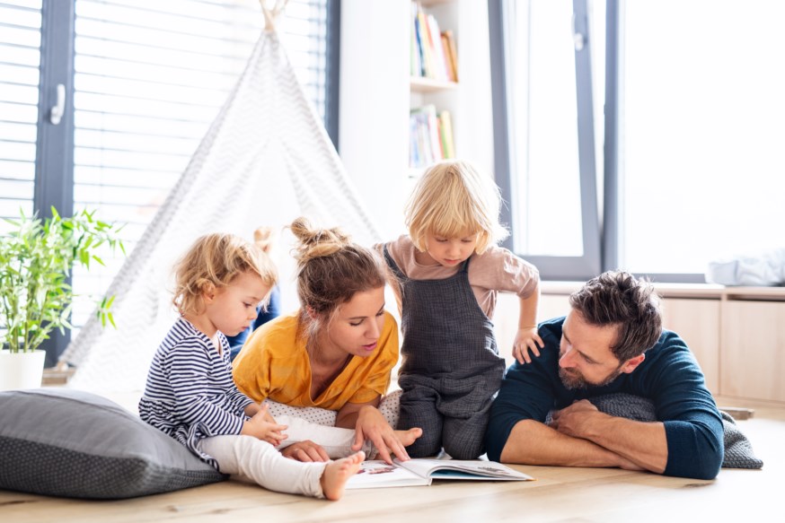 Familie på fire ligger å leser sammen på gulvet. Foto