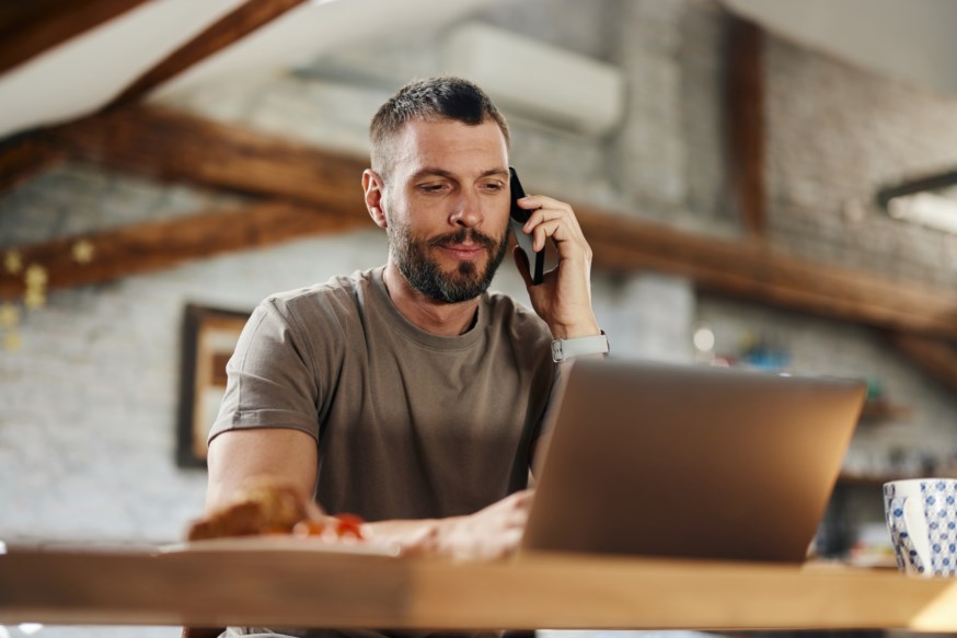 Mann sitter i telefon med pcen foran seg
