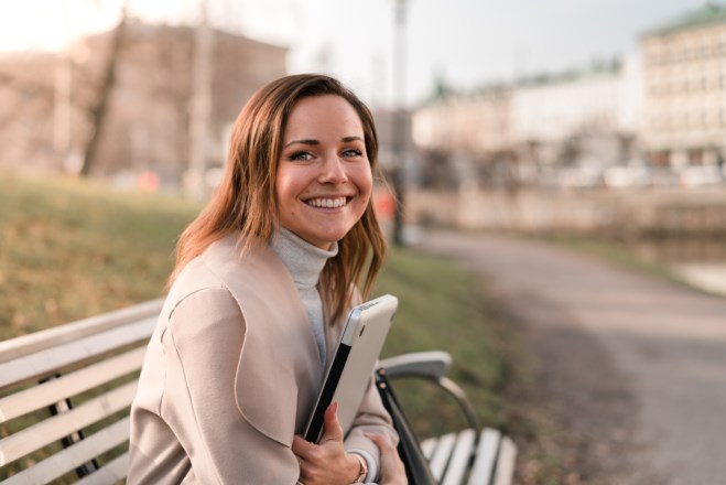 Kvinne smiler med PC i armene. Foto