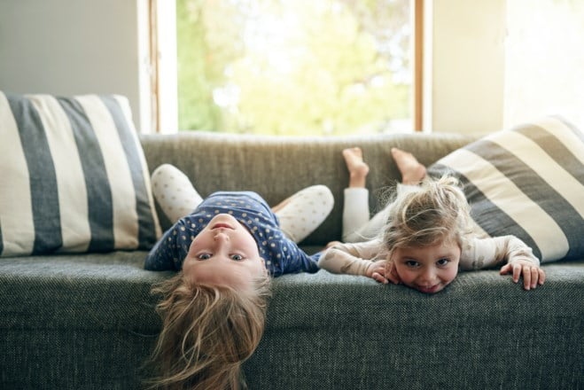 To små jenter ligger på sofaen. Foto