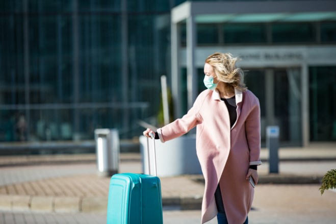 Kvinne på reise med munnbind og koffert. Foto. 