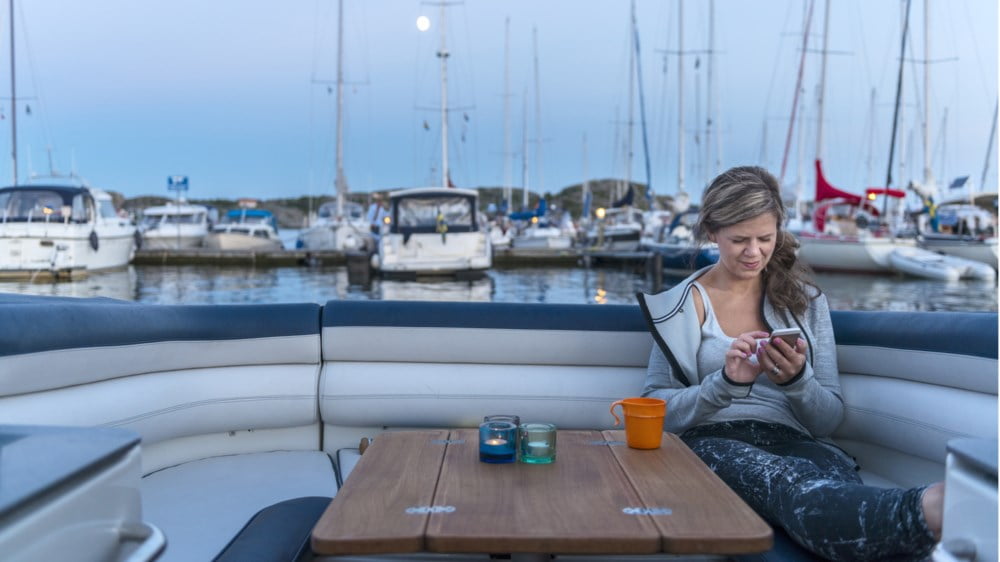 Dame med mobil sitter i seilbåt