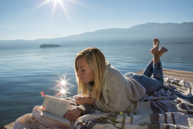 Dame leser bok på en brygge i solskinn